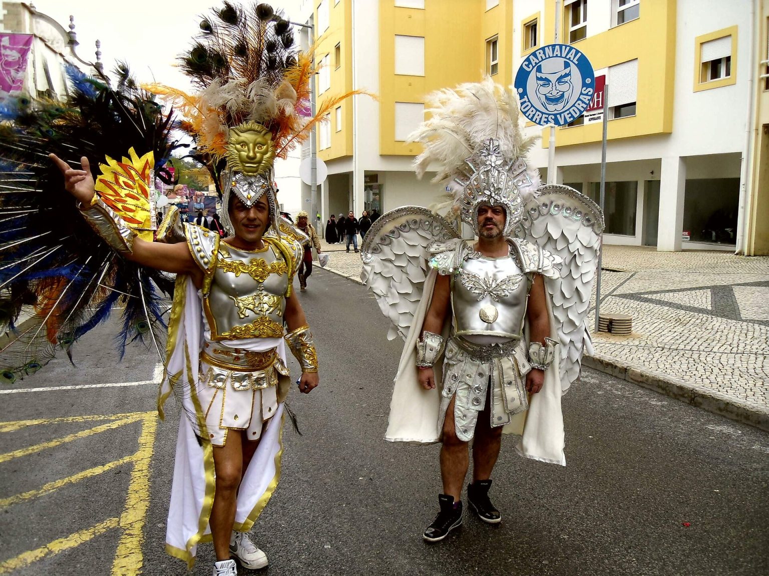 Two revellers in gladiator costumes and wings at the Torres Vedras Carnival, with the Carnival sign in the background