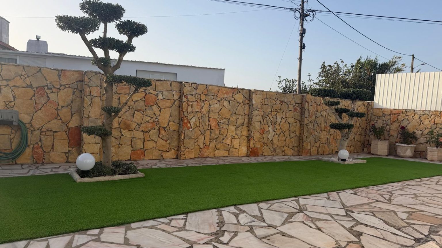 Relvado com oliveiras, candeeiros e muro de pedra no exterior da Dii Beach House