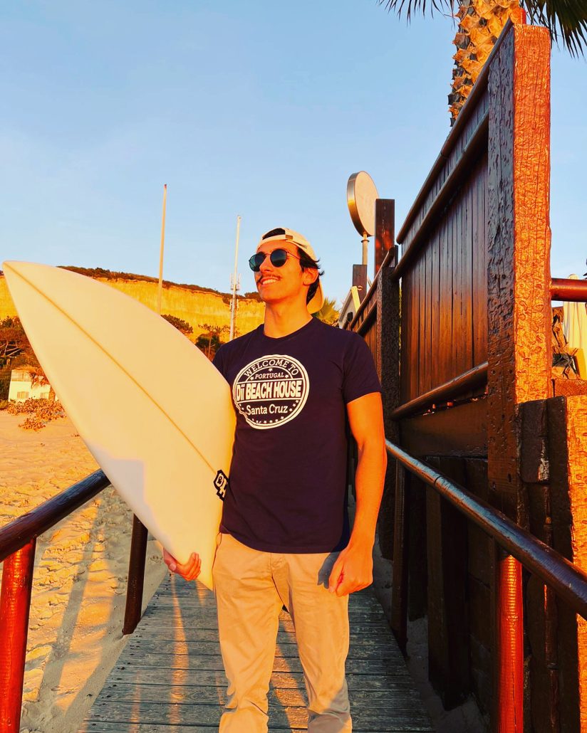 Surfer wearing a Dii Beach House T-shirt and board, at sunset