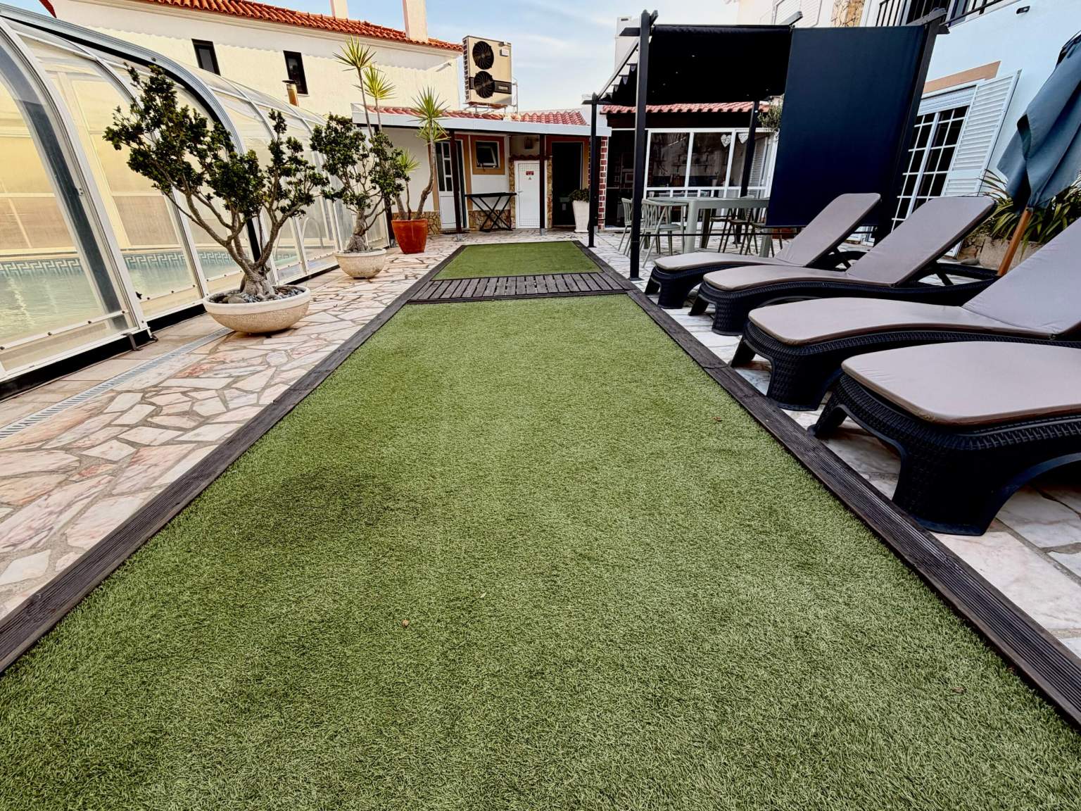 Jardim com relvado, espreguiçadeiras e piscina coberta